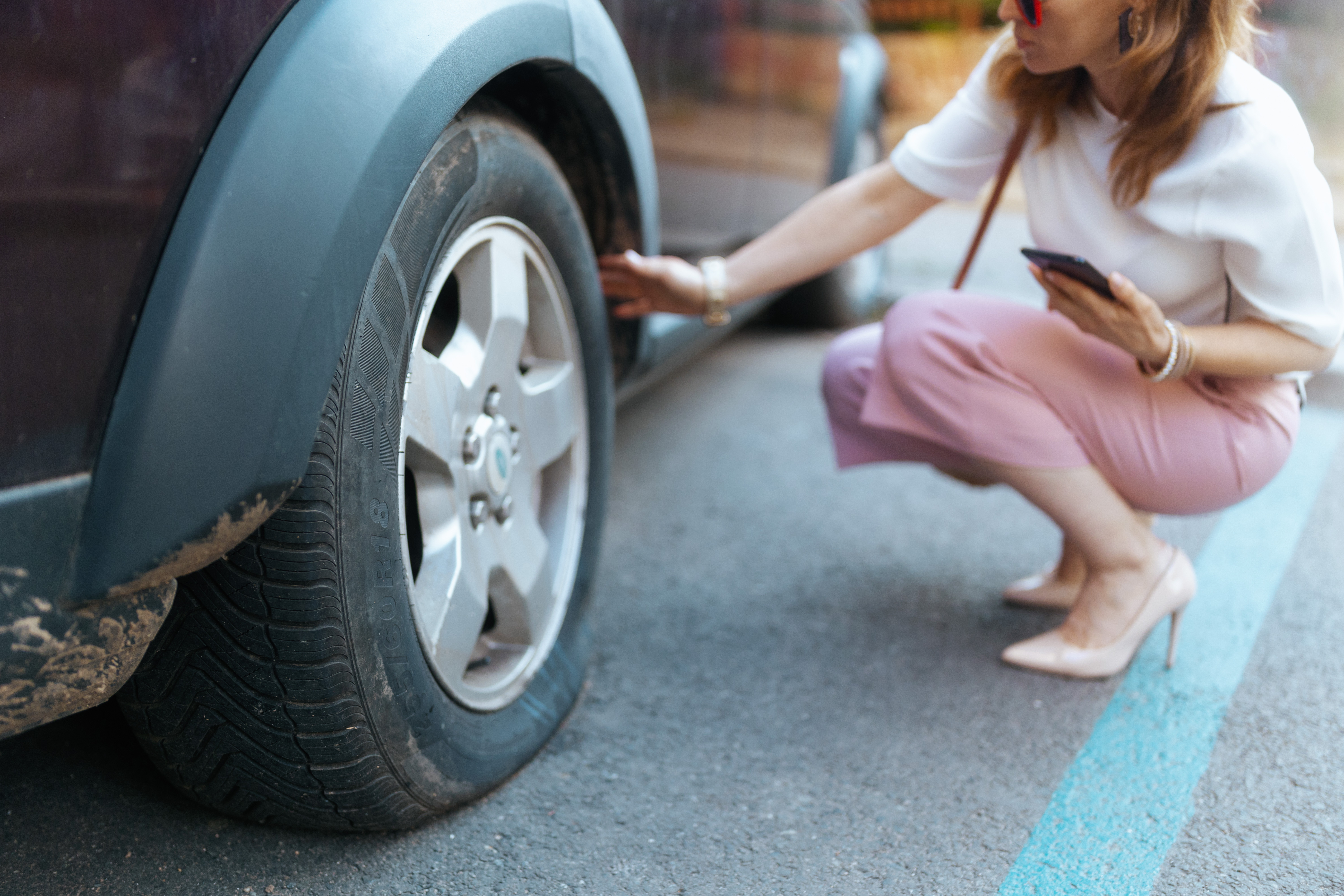 Closeup on woman in city with smartphone touching flat tire
